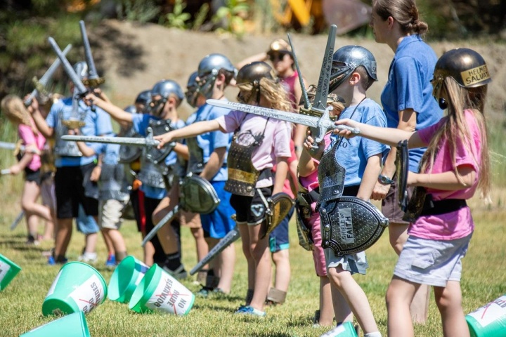 a group of children wearing pretend armor and holding plastic swords standing outdoors