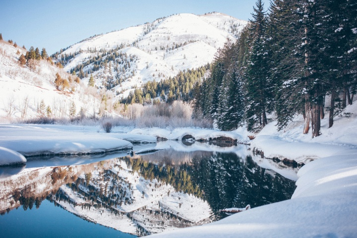 a winter mountain landscape with snow that is reflected in a body of water below