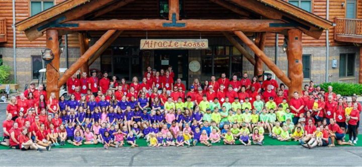 a large group of campers and staff standing under a wooden entryway labeled "miracle lodge."