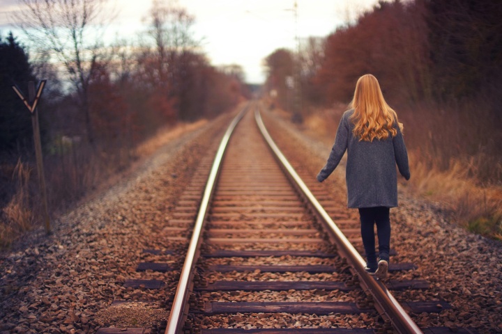 a woman walking beside a train track amidst autumn colors