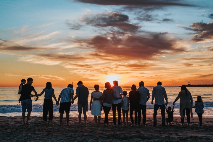 a group of people standing on the beach at sunset facing the ocean